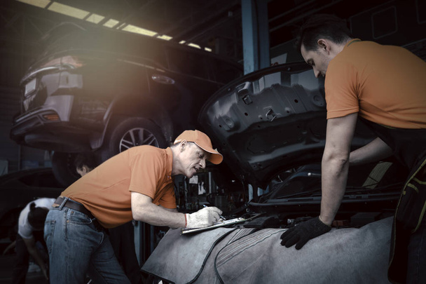 Garajda motorla çalışan iki tamirci, araba servisi teknisyeni otomobil hizmet merkezindeki müşteri arabasını kontrol edip onarıyor, araç tamirhanesi konsepti. - Fotoğraf, Görsel