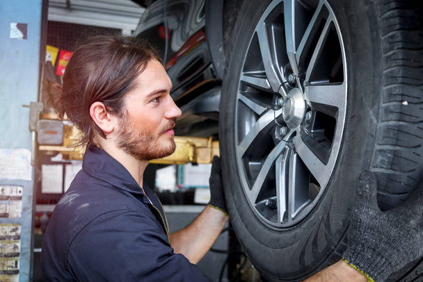 Auto mechanic working in garage, checking wheels, car service technician repairing customer car at automobile service center, inspecting car under body and suspension system, vehicle repair service shop. - Foto, Imagem