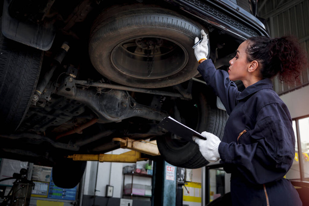 Female auto mechanic work in garage, car service technician woman check and repair customer car at automobile service center, inspecting car under body and suspension system, vehicle repair service shop. - Foto, afbeelding