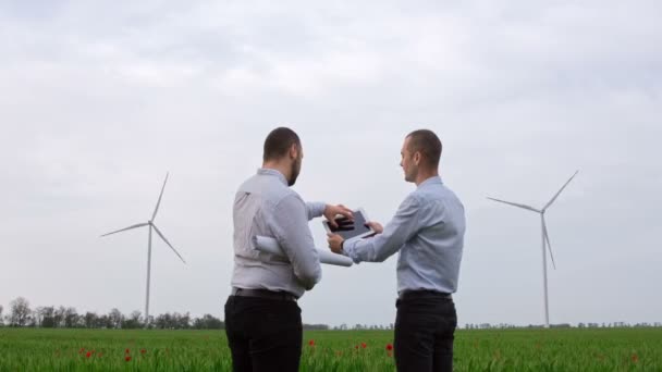Contrat pour l'installation de nouvelles éoliennes. Deux hommes parlent, discutent de dessins électroniques sur une tablette et se serrent la main debout dans un champ avec des éoliennes en arrière-plan.  - Séquence, vidéo