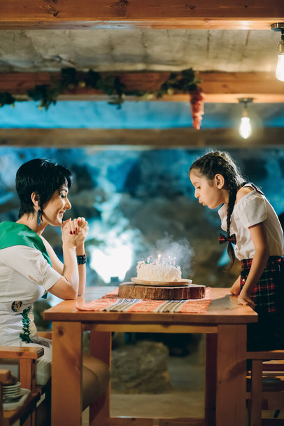 Young adorable schoolgirl celebrating her birthday with her mother and blowing out birthday candles - Photo, Image