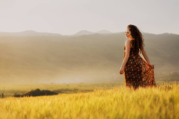 Armenian curly haired girl holding her dress in field and enjoying the sunshine - Fotoğraf, Görsel