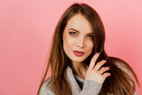 Close-up beauty portrait of a woman weared grey sweater on pink background. Professional model posing in studio. Lifestyle of caucasian happy girl - Photo, image