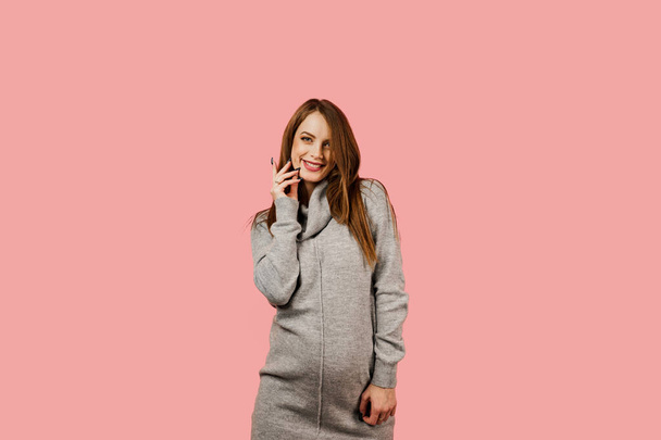 Pregnancy of a happy beautiful girl in a gray sweater on a pink background. Pregnant woman. Expectation of the child. Maternity leave. - Photo, Image