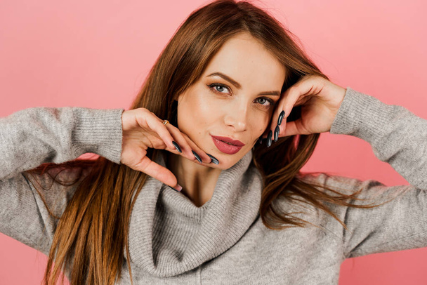 Close-up beauty portrait of a woman weared grey sweater on pink background. Professional model posing in studio. Lifestyle of caucasian happy girl - Photo, Image