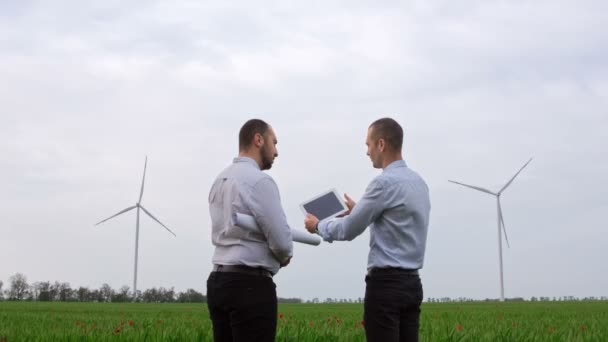 チーフエンジニアは、 2つの風車の背景に立って、曇りの天候での風力発電機の成功を同僚に証明します。. - 映像、動画
