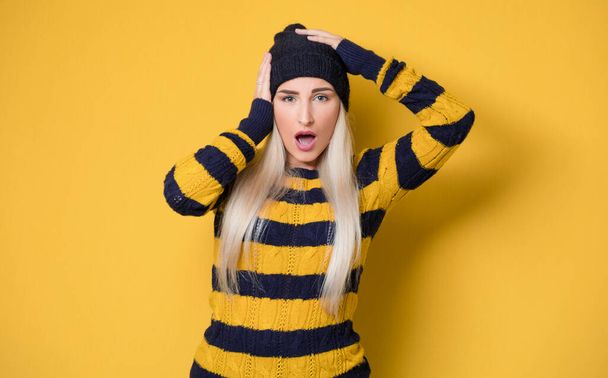 Panicking young woman stare to you, model wearing woolen cap and sweater, isolated on yellow background. Mistake. Bad news. Studio shot - Foto, Imagen