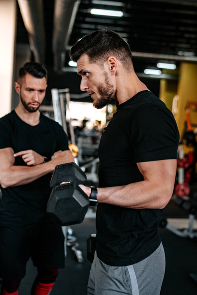 Portrait of male personal trainer helping out and assisting clients in the gym. Fitness details of healthy life, dumbbell training - Foto, afbeelding