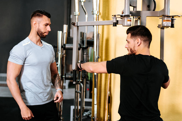 Handsome man doing weight exercises with assistance of his personal trainer at gym. Personal trainer fitness concept - Zdjęcie, obraz