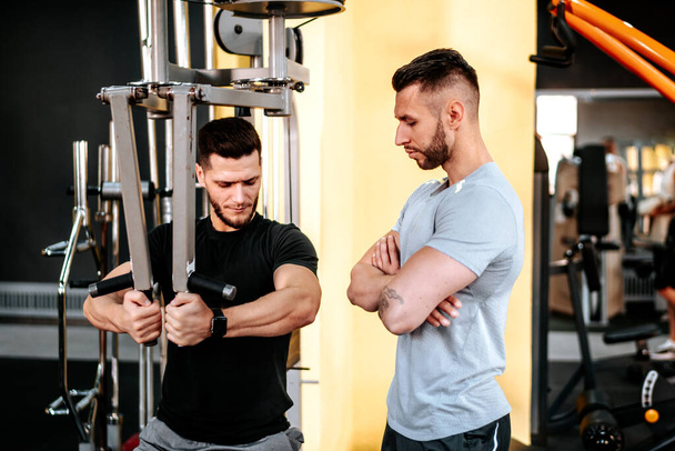 Handsome man doing chest exercises with assistance of his personal trainer at gym. - Valokuva, kuva