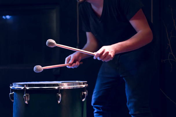 Der Percussionist spielt mit Stöcken auf dem Boden in einem dunklen Raum mit schönem Licht. Konzert- und Aufführungskonzept. - Foto, Bild