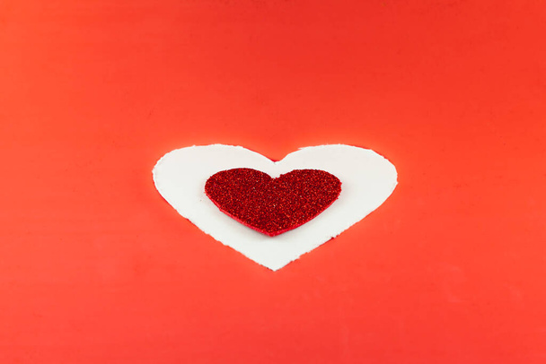 Em um fundo vermelho há um coração de papelão branco e dentro dele há um coração de brilho vermelho menor. Para o Valentine. - Foto, Imagem