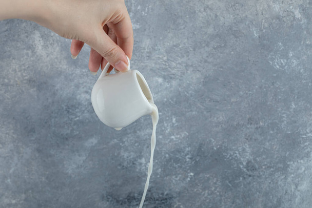 Γυναικείο χέρι ρίχνει φρέσκο γάλα από τη μικρή κούπα - Φωτογραφία, εικόνα
