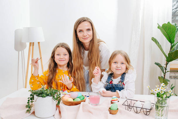 Mother and her two daughters posing for a photo, they all painting easter eggs - Foto, imagen