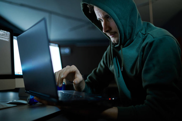 man internet hacker in kap werkt op laptop - Foto, afbeelding