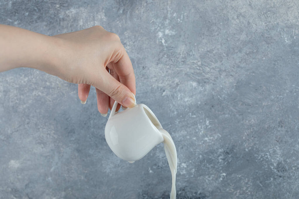 Dłoń kobiety wylewa świeże mleko z małego kubka - Zdjęcie, obraz