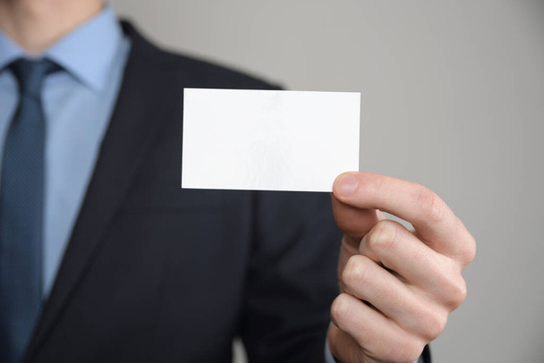 Empresario, la mano del hombre de negocios que muestra la tarjeta de visita - tiro de cerca sobre fondo gris. Muestra un pedazo de papel en blanco. Tarjeta de visita de papel. - Foto, imagen