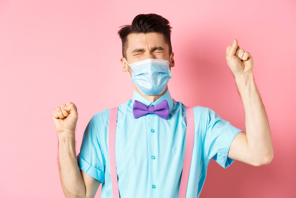 Coronavirus, salud y concepto de cuarentena. Hombre frustrado en máscara médica quejándose, dándose la mano y llorando de fracaso, de pie sobre fondo rosa - Foto, Imagen