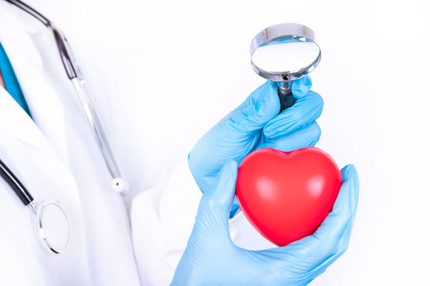 Professional medical doctor holding a magnifying glass check up on a red heart ball. Concept of health care. - Foto, Imagem