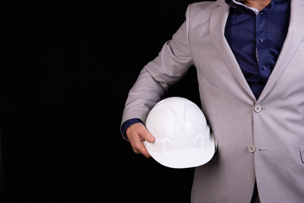 Ingenieur, bouwer, zakenman met een witte helm op een donkere achtergrond. Portret. Het concept techniek, bedrijfsleven, bouw, stadsleven en de toekomst. - Foto, afbeelding