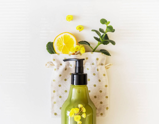The concept of cosmetics based on natural ingredients. A bottle of bath cosmetics with lemon, flowers and a green twig on a white background. Plant-based beauty products. Natural hand care product - Photo, image