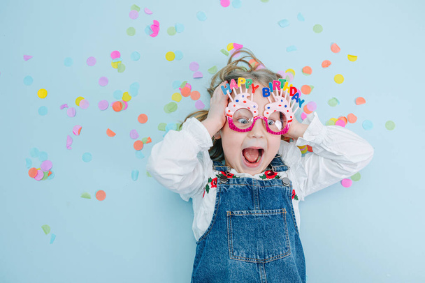 Funny little birthday girl lies on a floor with a confetti pieces - Fotografie, Obrázek