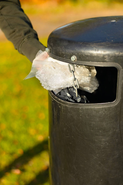 Wolontariusz wyrzucający plastikowe śmieci do kosza na śmieci w parku - Zdjęcie, obraz