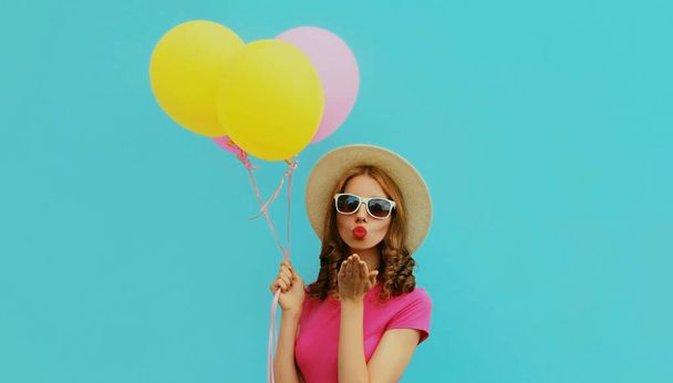 Portrait of beautiful young woman with bunch of colorful balloons blowing her lips sending sweet air kiss on a blue background - Fotografie, Obrázek