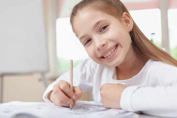 Close up of a beautiful happy schoolgirl smiling to the camera while drawing at school, copy space - 写真・画像