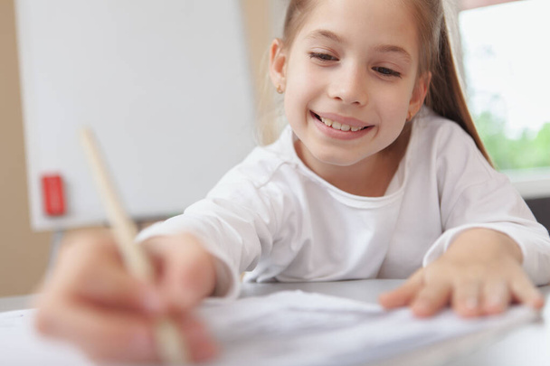 Cropped shot of a lovely happy young girl concentrating, drawing or writing in her textbook, copy space. Children education, development concept - Фото, изображение