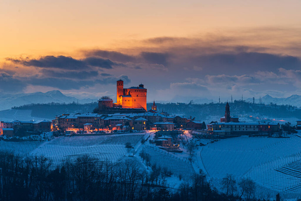Olaszország Piedmont: borudvar egyedülálló táj téli naplemente, Serralunga d 'Alba középkori falu megvilágított vár dombtetőn, az Alpok hófödte hegyek háttér, olasz örökség - Fotó, kép