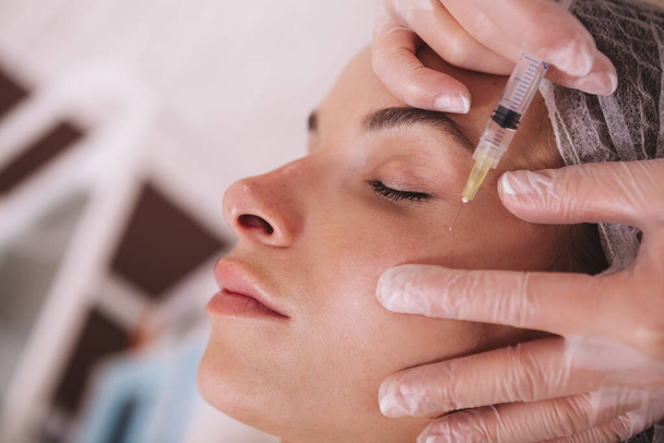 Cropped close up of a beautiful woman receiving anti-wrinkle treatment at beauty clinic. Professional beautician injecting face filler into skin of female client - Foto, immagini