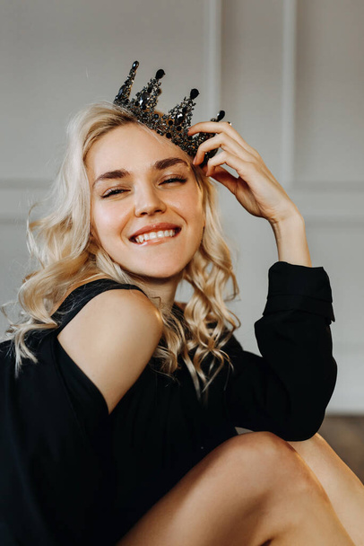 Happy young blonde woman with a crown, smiling, biting her lip, looking at camera. - Fotoğraf, Görsel