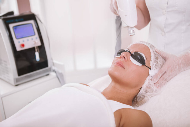 Mature woman getting facial laser treatment. Professional dermatologist removing skin pigmentation on a female patient - Foto, imagen