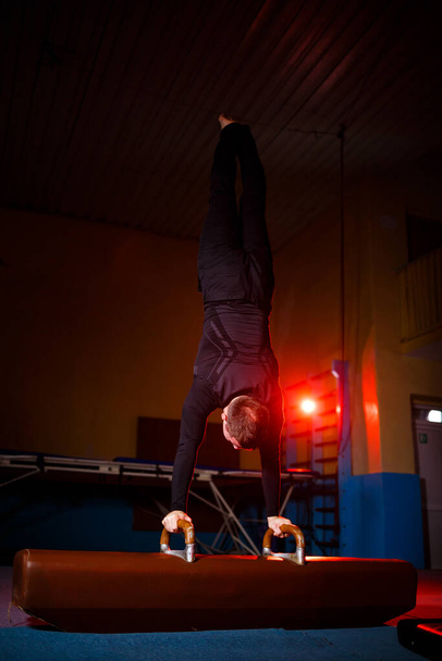 Взрослый мужчина в спортивной одежде делает упражнения на гимнастическом аппарате в акробатическом зале - Фото, изображение