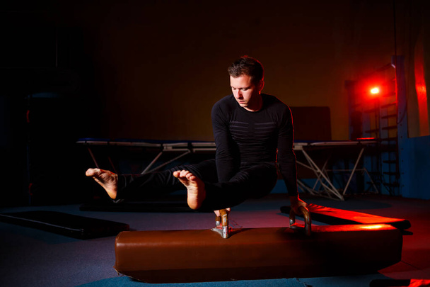 スポーツウェアの大人の男は、アクロバットジムで体操器具の練習を行う - 写真・画像