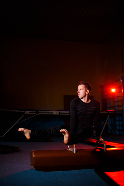 Spor giyimli yetişkin bir adam akrobatik spor salonunda jimnastik aletleri üzerinde egzersiz yapıyor. - Fotoğraf, Görsel