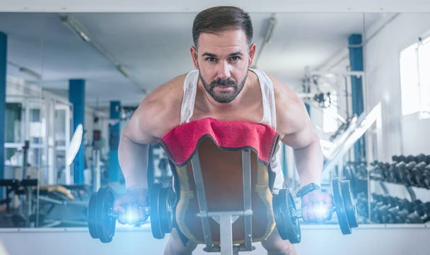 Un hombre haciendo ejercicios de brazo en el gimnasio acostado. Mirando a la cámara. Concepto de salud y bienestar - Foto, Imagen
