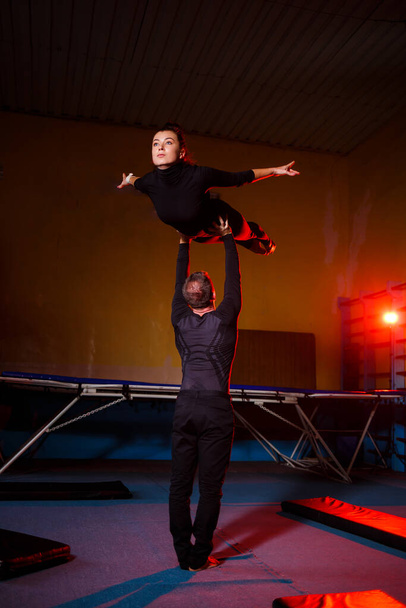 Duet akrobatów wykonujący sztuczkę podwójną. Kobieta w kombinezonie gimnastycznym i mężczyzna w odzieży sportowej. Bardzo elastyczni artyści cyrkowi. - Zdjęcie, obraz