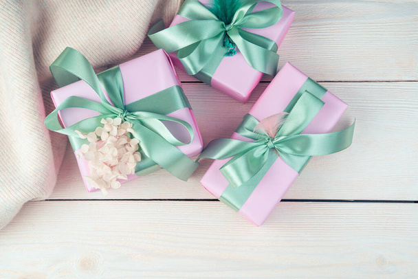 Tři růžové dárkové krabice se stuhami a svetrem na bílém dřevěném pozadí. - Fotografie, Obrázek