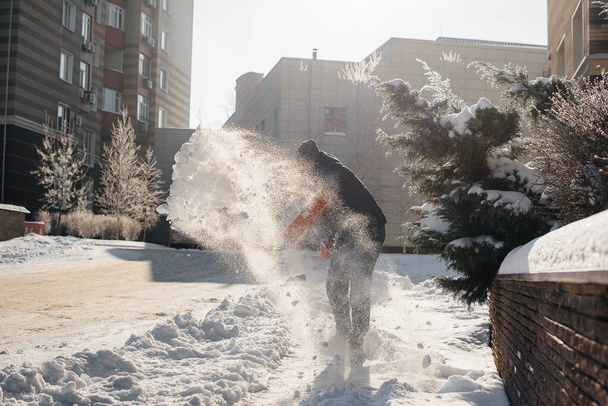 A young man clears the snow in front of the house on a sunny and frosty day. Cleaning the street from snow. - Φωτογραφία, εικόνα