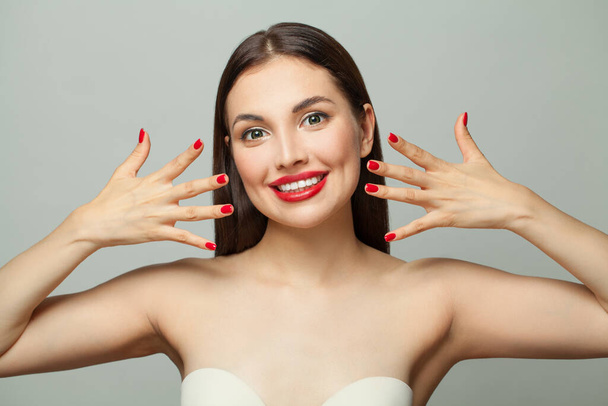 Счастливая молодая женщина с красными ногтями маникюра на белом фоне. Концепция ухода за телом и маникюра - Фото, изображение