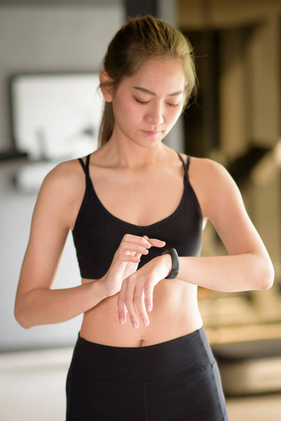An active woman is using smart watch in fitness gym. Fitness and technology concept . - Фото, изображение