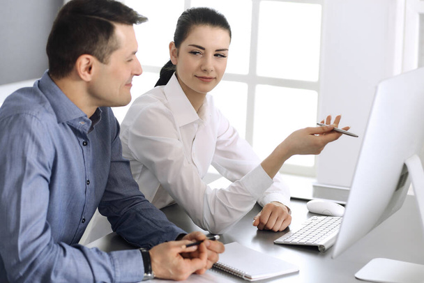 Cheerful smiling businessman and woman working with computer in modern office. Headshot at meeting or workplace. Teamwork, partnership and business concept - Photo, Image