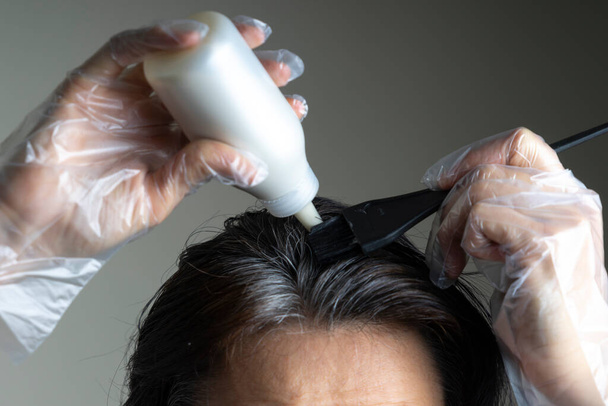 Gros plan femme mains teindre les cheveux à l'aide d'un pinceau noir. Femme d'âge moyen colorant les cheveux foncés avec des racines grises à la maison - Photo, image