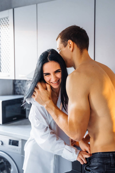 Lähikuva nauravasta rakastuneesta parista. Mies ja tyttö halaavat hellästi keittiössä. Esileikkiä ennen kuumaa seksiä öisin. Pilailemme, hymyilemme toisillemme pehmeässä, lämpimässä keltaisessa valossa. - Valokuva, kuva