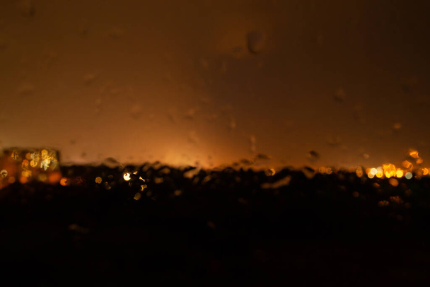 Regen und Blitze glühen hinter Glas unscharf. Nachtbeleuchtung in der Stadt - Foto, Bild