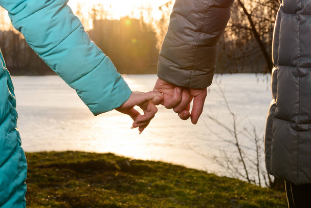 Guy with a girl holding hands walking in the park at sunset, a romantic evening before Valentine's Day. new - Photo, Image