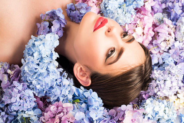 Nature beauty. Woman lying on flowers. Unity with nature. Blossom. Makeup cosmetics and skincare. Girl with hydrangea flowers. - 写真・画像