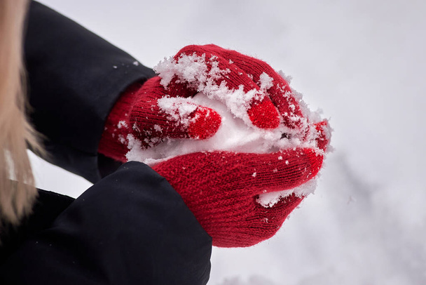 hands in red gloves make a snowball on the background of snow. winter entertainment, activities - Foto, Bild